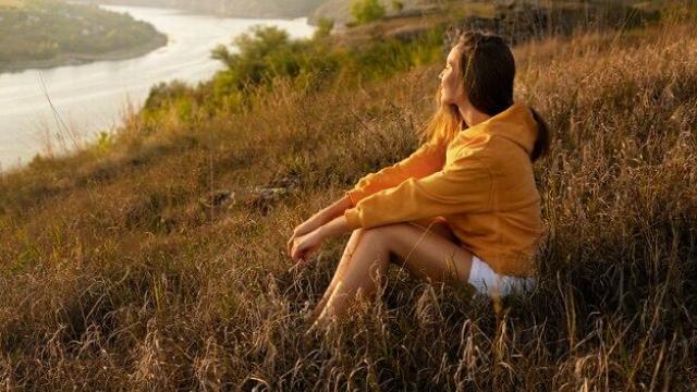Mujer sentado en la ladera mirando a un río